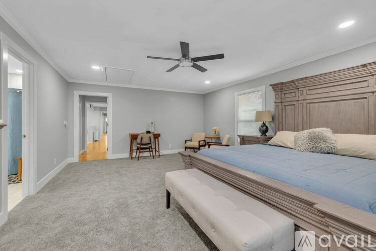 A bedroom with a bed, a chair, a table, and a ceiling fan.