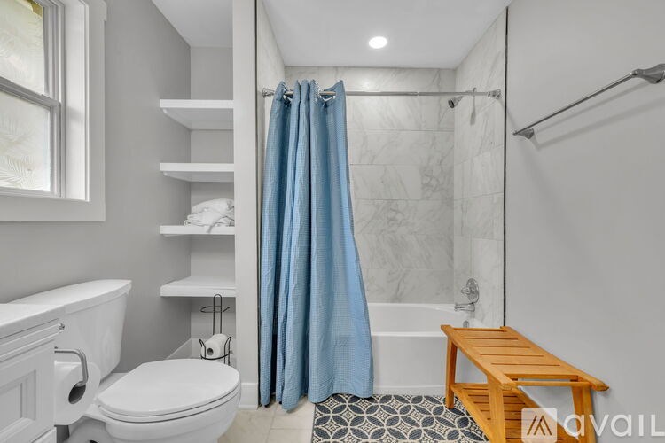 A bathroom with a white toilet, a white sink, a blue shower curtain, and a wooden bench.