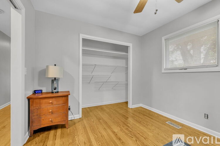 A room with a wooden floor, a ceiling fan, and a wooden table with a lamp and a clock on it.