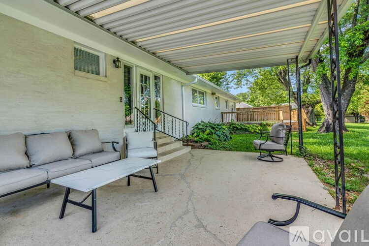 A patio with a couch, chairs, and a table is covered by a roof.