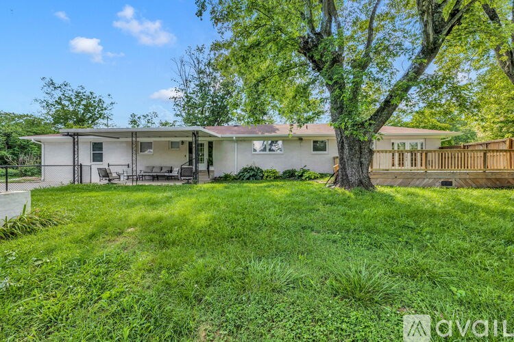A house with a white exterior and a brown fence is surrounded by green grass and trees.