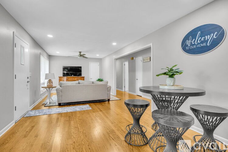 A living room with a grey sofa, a round table with four chairs, and a wall with a sign that says "welcome to our home".