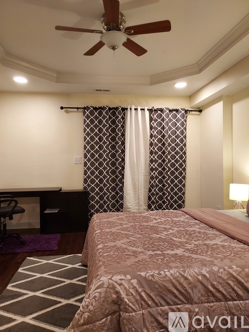 A bedroom with a bed, a fan, and a window with a curtain.