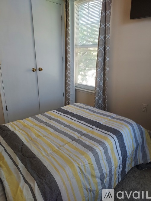 A bed with a striped comforter is in a room with a white door and a window with a curtain.