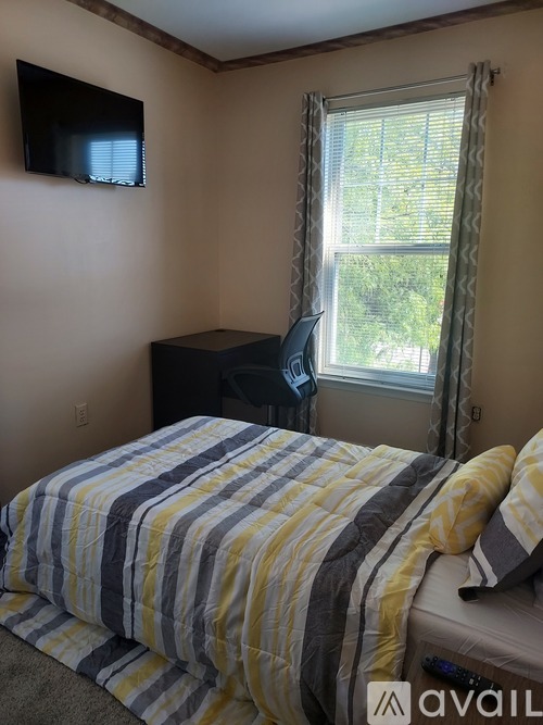 A bedroom with a bed, a television, and a window with a view of trees.