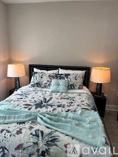 A bed with a floral patterned comforter and two matching pillows is flanked by two lamps on either side.