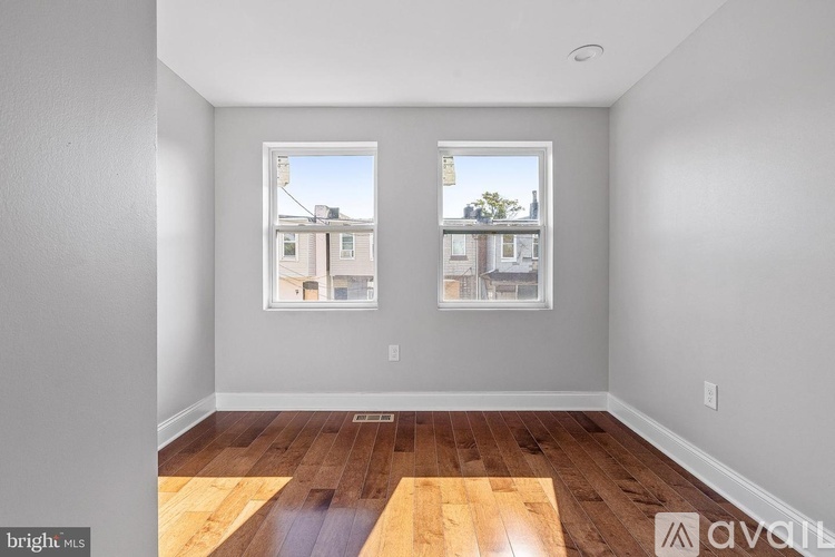 A room with wooden floors and two windows showing an outside view.