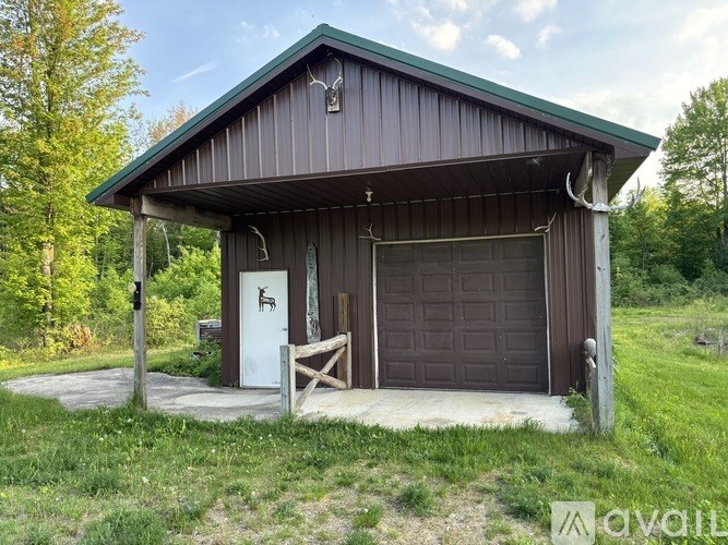 A garage with a brown roof and a white door is surrounded by grass and trees.
