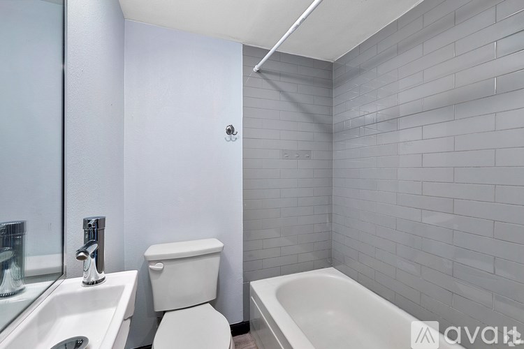 A white toilet sits next to a white sink in a bathroom with grey tiled walls.