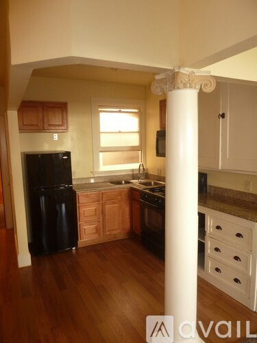 A kitchen with wooden floors and a black refrigerator.