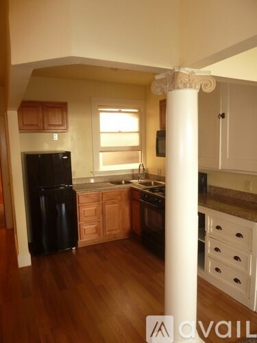 A kitchen with wooden floors and a black refrigerator.