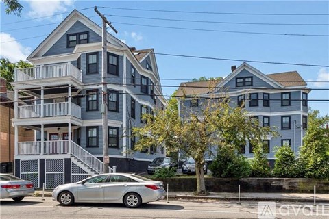 A silver car is parked in front of a two-story building with a balcony.
