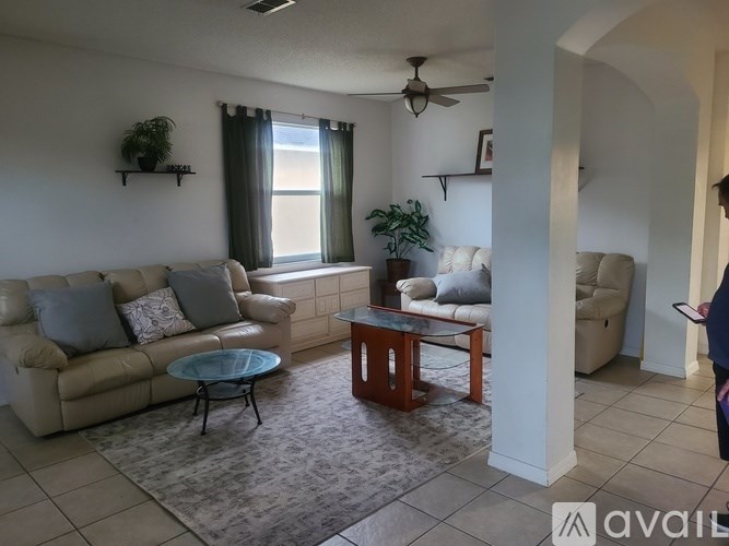 A living room with a beige couch, a glass coffee table, and a ceiling fan.