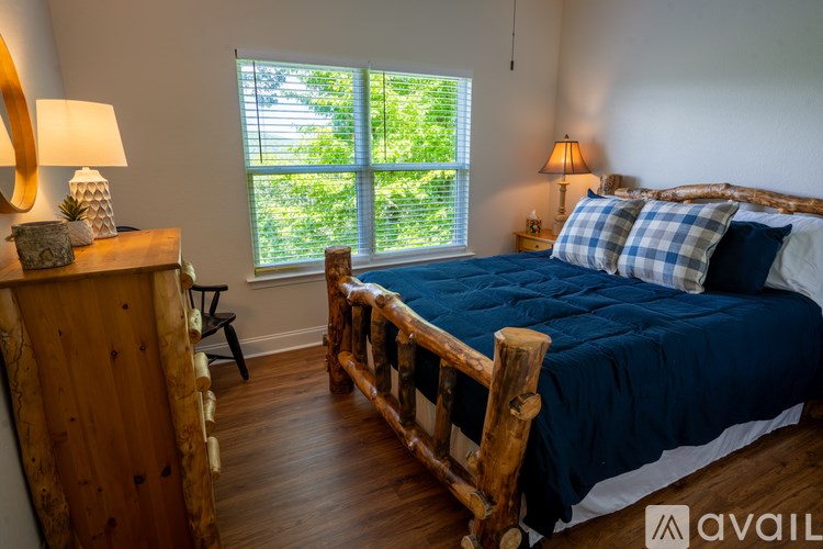 A bedroom with a bed, wooden dresser, and window with blinds.