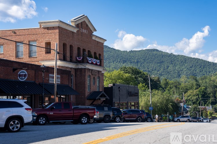 A street view of a town with cars parked on the side of the road and a mountain in the background.
