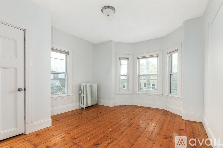 A room with wooden floors and white walls, with a window and a door.
