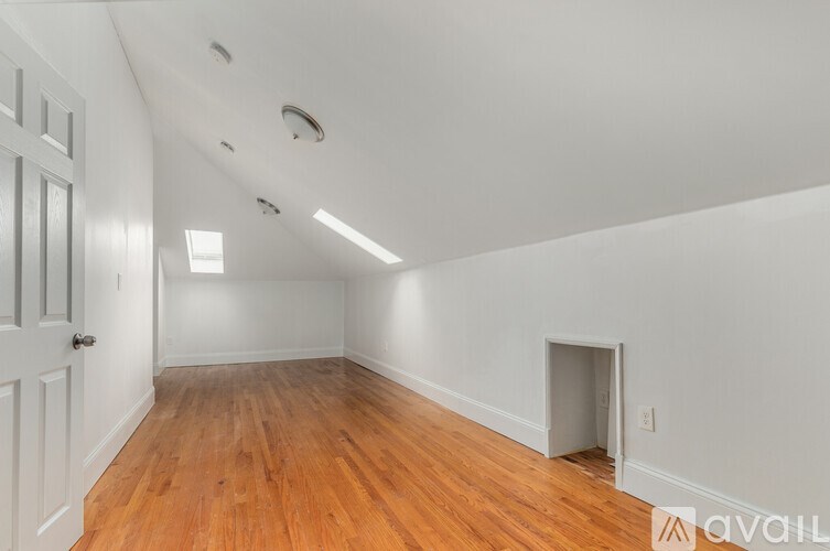 A room with wooden floors and white walls, with a door on the left and a small opening on the right.