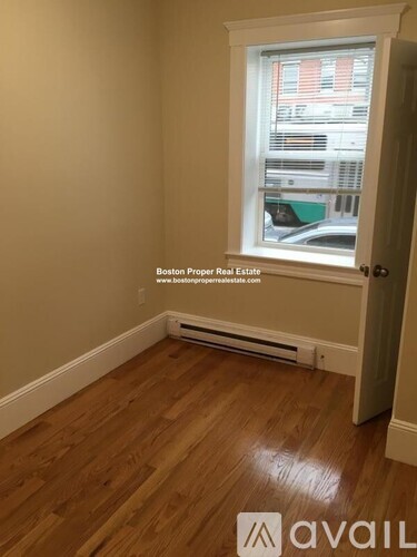 A room with wooden flooring and a window showing a view of a building outside.