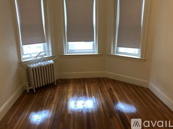 A room with wooden floors and three windows with blinds.