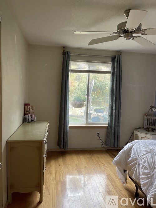 A room with a ceiling fan, a window with curtains, and a bed with white bedding.