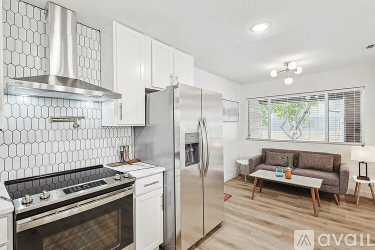 A modern kitchen with a stove top oven, refrigerator, and a couch in the living room.