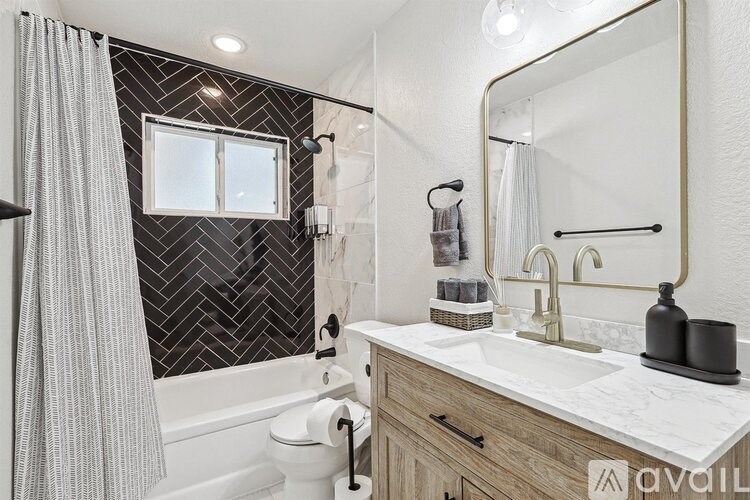 A bathroom with a white toilet, a sink with a gold faucet, a mirror, and a shower with a grey curtain.