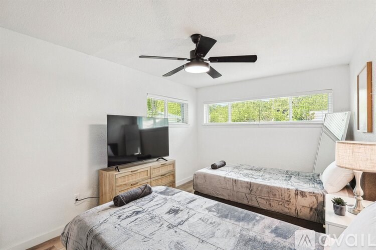 A bedroom with a bed, a television, and a ceiling fan.