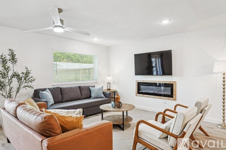 A living room with a grey couch, a brown leather couch, a wooden coffee table, a television, a fireplace, and a ceiling fan.