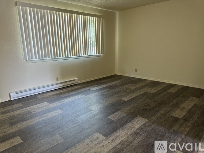A room with wooden flooring and a window with blinds.