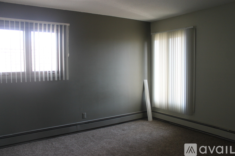 A room with a carpeted floor, a window with blinds, and a wall with a light switch.