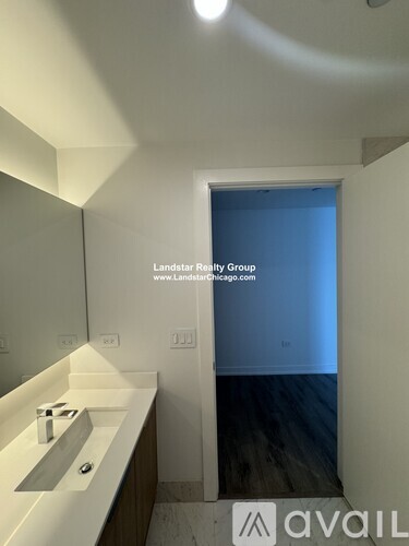 A bathroom with a sink and mirror in the foreground and a doorway leading to a bedroom in the background.
