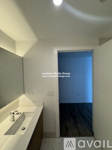 A bathroom with a sink and mirror in the foreground and a doorway leading to a bedroom in the background.