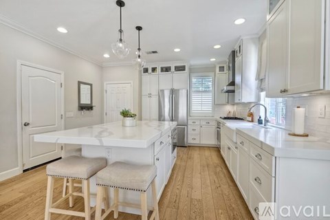 A kitchen with white cabinets and a white island with two stools.