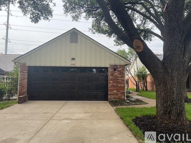 A garage with a black door is situated next to a large tree.