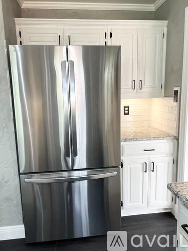 A stainless steel refrigerator in a kitchen with white cabinets.