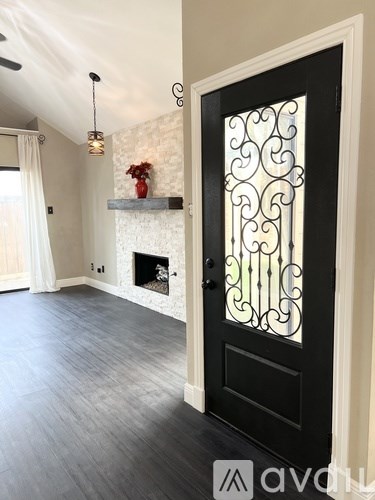A black door with a decorative glass panel is in a room with a fireplace and a vase of flowers.