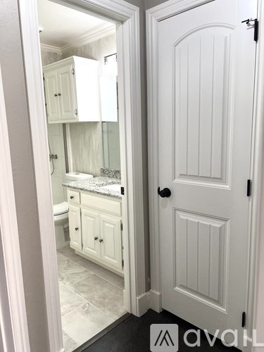 A white bathroom with a toilet, sink, and cabinets is shown.