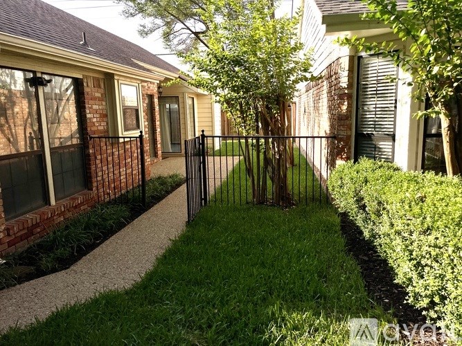 A black iron fence separates a grassy area from a brick building.