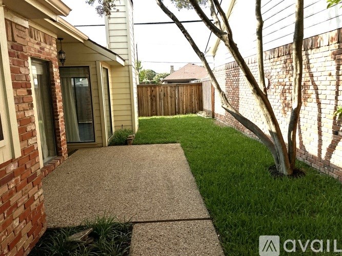 A backyard with a concrete pathway, a tree, and a brick wall.