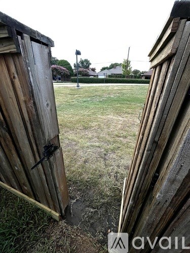 A wooden gate is open, revealing a grassy field.