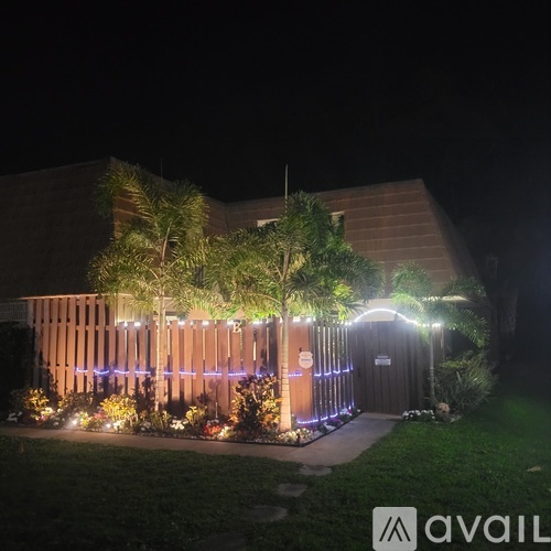 A building is lit up at night with a wooden fence and trees in front.