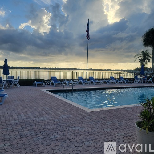 A pool area with a flag pole and chairs overlooking a body of water.