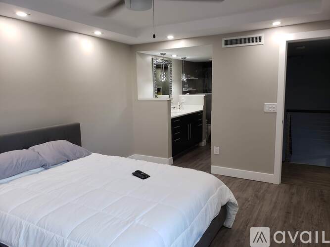A bedroom with a large bed and a small kitchen area in the background.