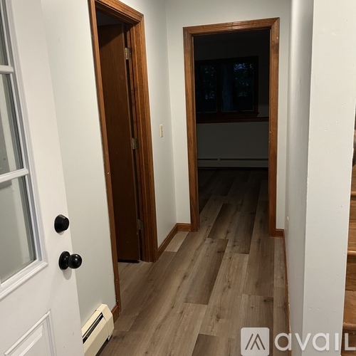 A hallway with a wooden door and a white door with a window.