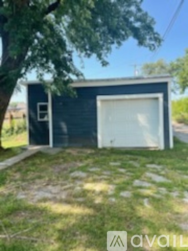 A small blue building with a white door is situated in a grassy area.