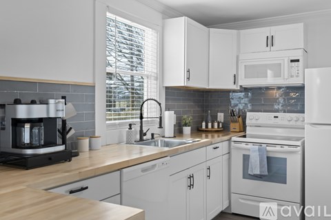 A kitchen with white cabinets and appliances, a wooden countertop, and a window with blinds.