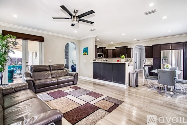 A spacious living room with a brown leather couch and a ceiling fan.