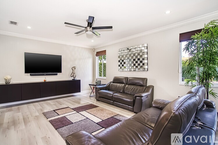 A living room with a black leather couch and a flat screen TV mounted on the wall.
