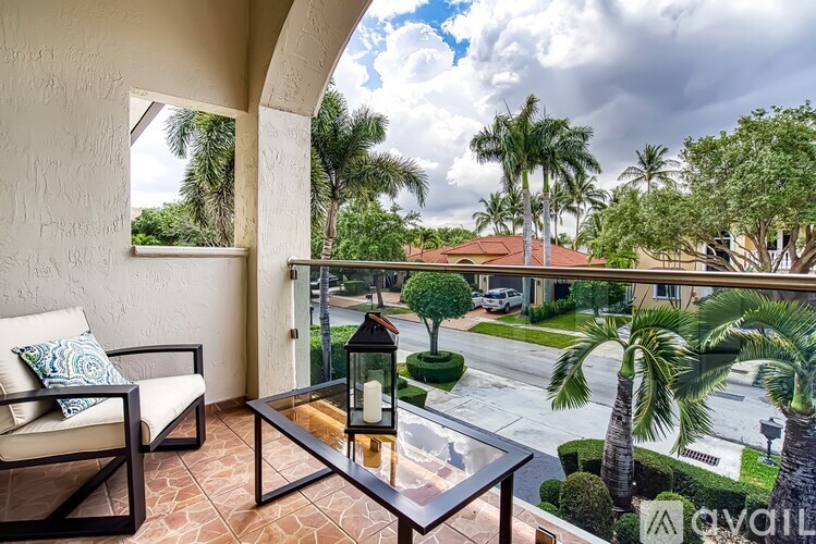 A balcony with a table and chairs overlooking a street with palm trees.
