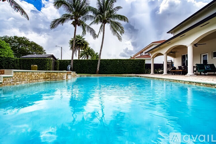 A swimming pool surrounded by a house and palm trees.